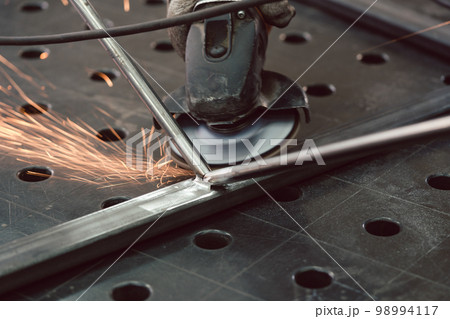 Worker in metal factory grinding workpiece with sparks flying 98994117