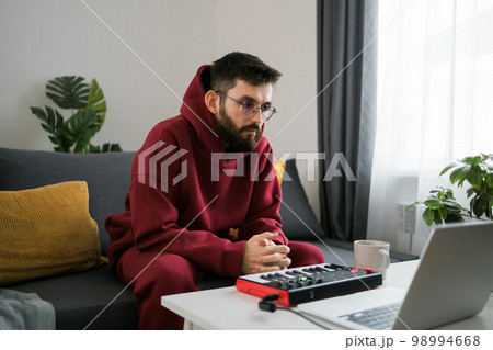 Man music producer or arranger using laptop and midi keyboard and other audio equipment to create music at home studio. Beat making and arranging audio content and composing song concept 98994668