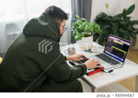 Man music producer or arranger using laptop and midi keyboard and other audio equipment to create music at home studio. Beat making and arranging audio content and composing song concept Man music producer or arranger using laptop and midi keyboard and other audio equipment to create music at home studio. Beat making and arranging audio content and composing song concept 98994687