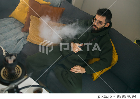 Bearded man is smoking hookah at home and blowing cloud of smoke - chill time and resting concept 98994694