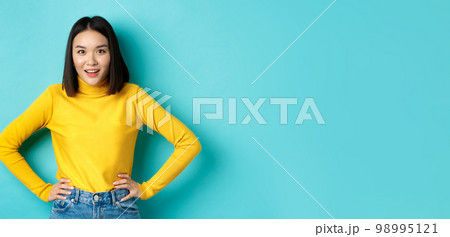 Image of impressed korean girl listening interesting story, looking at camera intrigued, standing over blue background 98995121