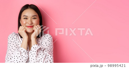 Beauty and lifestyle concept. Close-up of adorable asian woman showing puffy cheeks, smiling and looking happy, standing over pink background Beauty and lifestyle concept. Close-up of adorable asian woman showing puffy cheeks, smiling and looking happy, standing over pink background 98995421