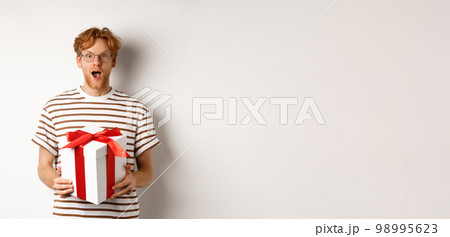 Valentines day and holidays concept. Surprised redhead boyfriend in glasses looking grateful at camera, receive big present in box, standing over white background 98995623