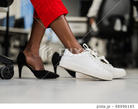 African woman changing from high heels to sneakers in the office. Tired legs.  98996185