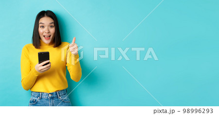 E-commerce and online shopping concept. Excited and amazed asian woman showing thumbs up after using smartphone app, recommend device, standing over blue background E-commerce and online shopping concept. Excited and amazed asian woman showing thumbs up after using smartphone app, recommend device, standing over blue background 98996293