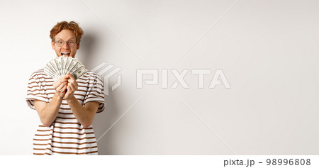 Shopping and finance concept. Lucky redhead guy winning, showing prize money and smiling happy, standing in glasses and t-shirt over white background 98996808