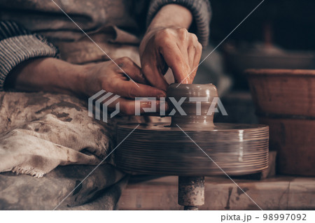 Modeling bowl from clay on wheel in pottery workshop. Dirty hands of craftsman mold crockery. Shaping pot. Modeling bowl from clay on wheel in pottery workshop. Dirty hands of craftsman mold crockery. Shaping pot. 98997092