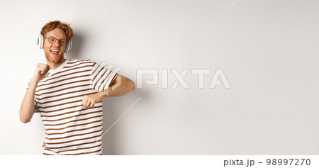 Technology concept. Happy redhead man listening music in headphones and dancing cheerful, standing in t-shirt against white background 98997270