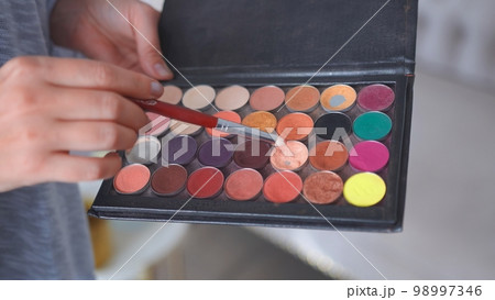 Makeup artist holds shadows in his hand and paints a model. Makeup artist holds shadows in his hand and paints a model. 98997346