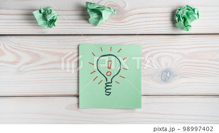 Flat lay of green sticker note with light bulb and red exclamation mark inside near crumpled notes. Idea, creative work. 98997402