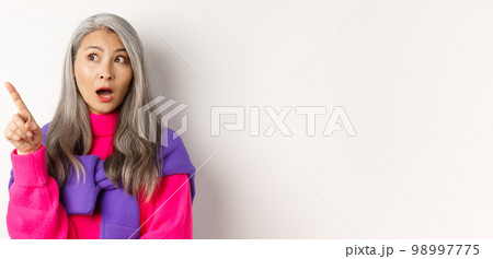 Curious asian senior woman pointing at something interesting, looking at promo wondered, standing in trendy outfit over white background 98997775