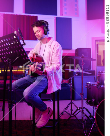 Musician, headphones or guitar in neon studio, recording production or performance on radio mic, label or band concert. Guitarist, artist or man playing on strings instrument in night light practice 98999111