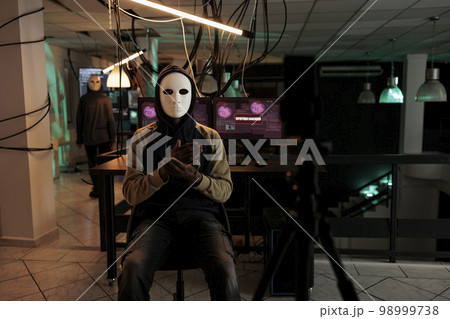 Ransomware and internet blackmail concept at night, anonymous scammer recording threat video on smartphone. Hacker stealing database online, computer network malware and cybercrime. Ransomware and internet blackmail concept at night, anonymous scammer recording threat video on smartphone. Hacker stealing database online, computer network malware and cybercrime. 98999738