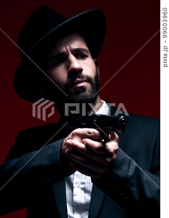 Assassin, suit or shooting weapon on studio background in dark secret spy, isolated mafia leadership or crime security. Model, gangster or hitman gun in aim, formal style or fashion clothes aesthetic 99003960