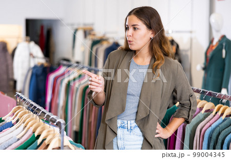 Young positive female shopper examining warm sweaters in women cloths shop Young positive female shopper examining warm sweaters in women cloths shop 99004345