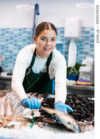 Female seller in apron shows hands fish trout on counter in supermarket 99004606