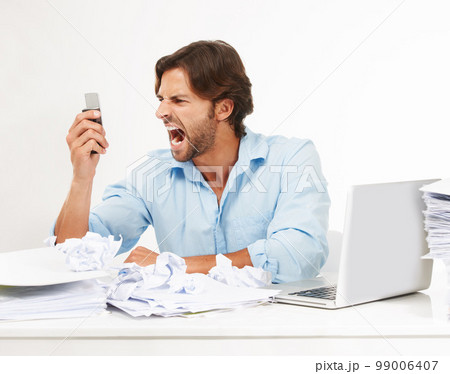 Angry, frustrated business man scream into phone in studio for fail, problem or debt stress at his desk. Rude, chaos and upset worker with technology, paper and computer isolated on white background 99006407