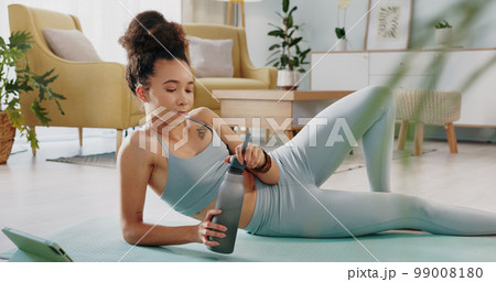 Fitness, relax and woman drinking water in living room with tablet streaming online class for workout, health and exercise. Yoga, internet or e learning with athlete in home gym training for wellness Fitness, relax and woman drinking water in living room with tablet streaming online class for workout, health and exercise. Yoga, internet or e learning with athlete in home gym training for wellness 99008180