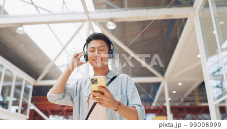 Phone, music headphones and Asian man walking in mall streaming podcast or radio. Technology, travel and happy male listening to song, audio sound or playlist on mobile smartphone in urban building. Phone, music headphones and Asian man walking in mall streaming podcast or radio. Technology, travel and happy male listening to song, audio sound or playlist on mobile smartphone in urban building. 99008999
