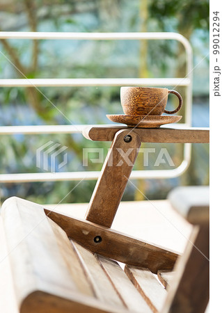 Handcraft bamboo cup of coffee or tea in sunlight. Summer morning on balcony. 99012294