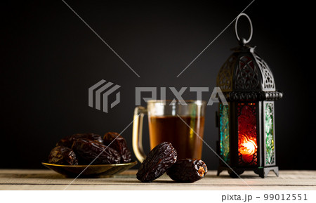 Ramadan food and drinks concept. Ramadan Lantern with arabian lamp, wood rosary, tea, dates fruit and lighting on a wooden table with dark background. Ramadan food and drinks concept. Ramadan Lantern with arabian lamp, wood rosary, tea, dates fruit and lighting on a wooden table with dark background. 99012551
