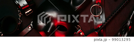 Set of toys from a sex shop on a dark background. Mask, leather belt, choker, handcuffs, whip and anal plug 99013295