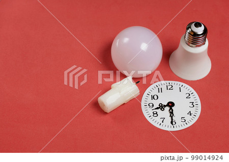 Disassembled LED bulb. Nearby is a candle stub. Clock face with arrows at 20 99014924
