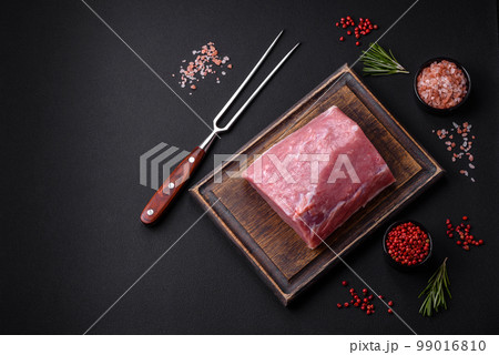A piece of raw fresh pork on a wooden cutting board with spices and herbs A piece of raw fresh pork on a wooden cutting board with spices and herbs 99016810