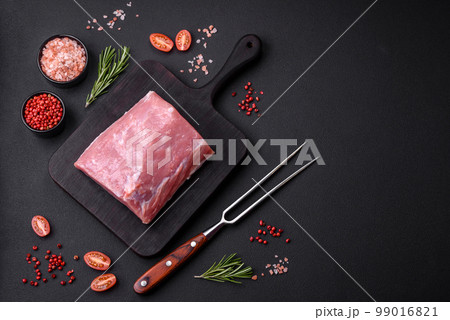 A piece of raw fresh pork on a wooden cutting board with spices and herbs A piece of raw fresh pork on a wooden cutting board with spices and herbs 99016821