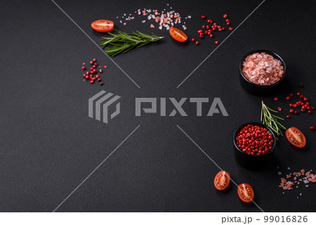 Ingredients salt, spices, herbs and tomatoes on a dark concrete background 99016826