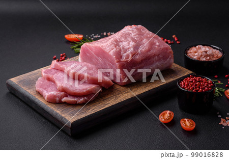 A piece of raw fresh pork on a wooden cutting board with spices and herbs 99016828