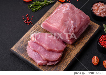 A piece of raw fresh pork on a wooden cutting board with spices and herbs 99016829