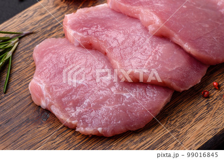 A piece of raw fresh pork on a wooden cutting board with spices and herbs A piece of raw fresh pork on a wooden cutting board with spices and herbs 99016845