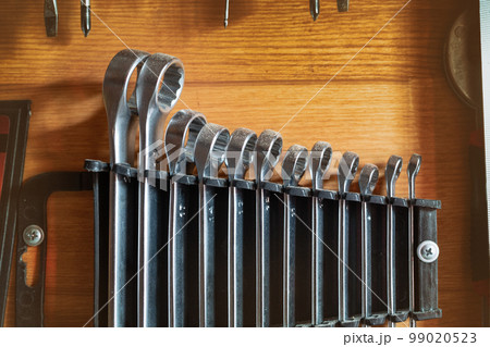 Set of used metal steel ring wrench organized and hanged in plastic holder against wooden wall. Workshop spanner tools and equipment industrial background. Garage workshop toolkit 99020523