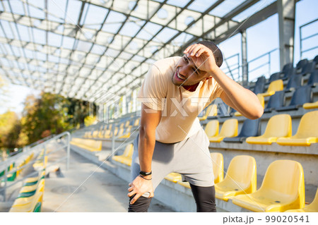 Tired hispanic athlete bent over and breathing after jogging, man doing sports on sunny day with active exercises and fitness, athlete resting after jogging. 99020541