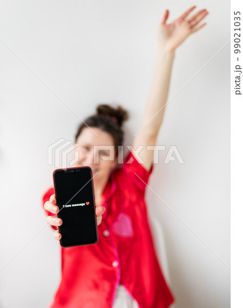 A happy girl is holding a smartphone with an activated screen with 1 SMS message in the shape of a heart. Concept of Valentine's Day, February 14. 99021035
