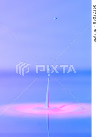 A drop falls into a thick liquid with a blue-pink background. Abstract colorful background. 99022360
