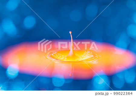 The drop falls into a dense liquid with a blue-yellow background. Abstract colorful background. 99022364
