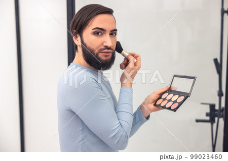 Serious man looking at the mirror during the blush application Serious man looking at the mirror during the blush application 99023460