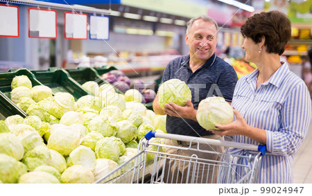 Mature family of retirees examines head of cabbage in grocery section of the supermarket Mature family of retirees examines head of cabbage in grocery section of the supermarket 99024947