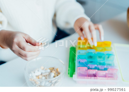 Woman's hands sorting pills into pills organizer. Close up medical pill box with daily doses of medicines. Antioxidant diet vitamin supplements for health and beauty care, biohacking concept. 99027561