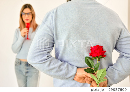 A man holding a red rose behind his back . A man holding a red rose behind his back . 99027609
