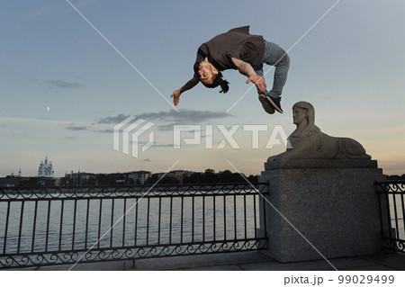 Young sporty man doing backflip in city 99029499