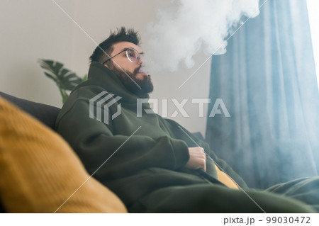 Bearded man is smoking hookah at home and blowing cloud of smoke - chill time and resting concept 99030472