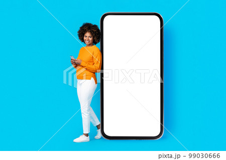 Cheerful black woman standing by huge phone white screen, mockup Cheerful black woman standing by huge phone white screen, mockup 99030666