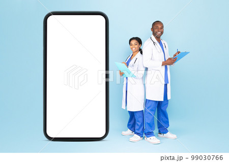 Telehealth concept. Happy male and female doctors in uniform standing near huge blank smartphone, mockup 99030766