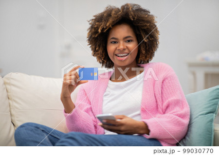 Positive attractive black woman showing credit card, using phone Positive attractive black woman showing credit card, using phone 99030770