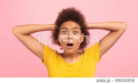 Shocked emotional young black curly woman screaming with open mouth, hold hand with hands Shocked emotional young black curly woman screaming with open mouth, hold hand with hands 99030958