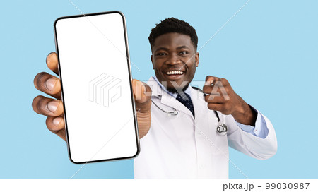 African American Male Doctor In Uniform Pointing At Smartphone With Blank Screen African American Male Doctor In Uniform Pointing At Smartphone With Blank Screen 99030987