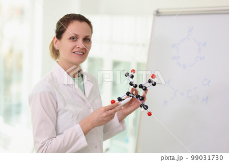 Female scientist standing near whiteboard, pointing to molecular model in her hand. Female scientist standing near whiteboard, pointing to molecular model in her hand. 99031730